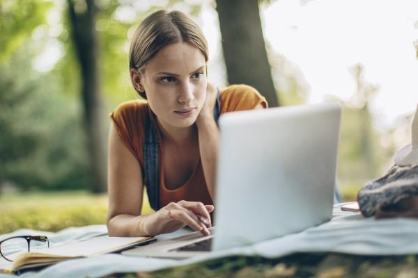 woman on computer laying on grass in park