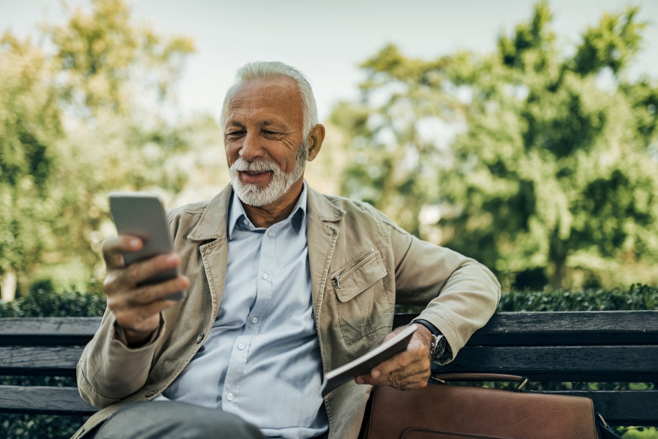 Old guy looking at his phone, sitting on a bench