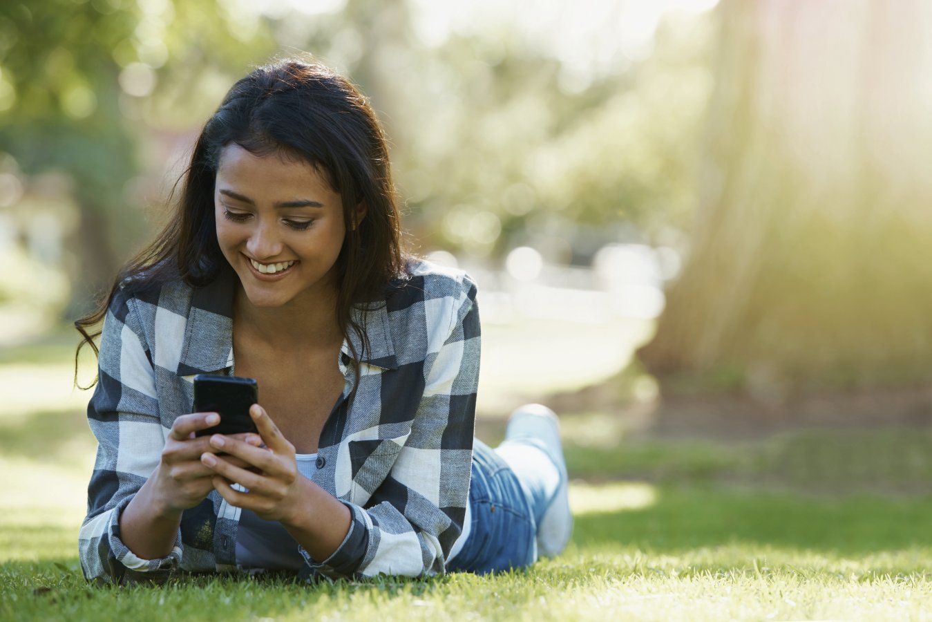 woman laying on grass, checking her phone